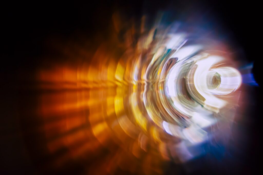 Abstract image featuring a radial blur of bright blue and orange colors, creating a dynamic swirling effect centered around a bright white light.