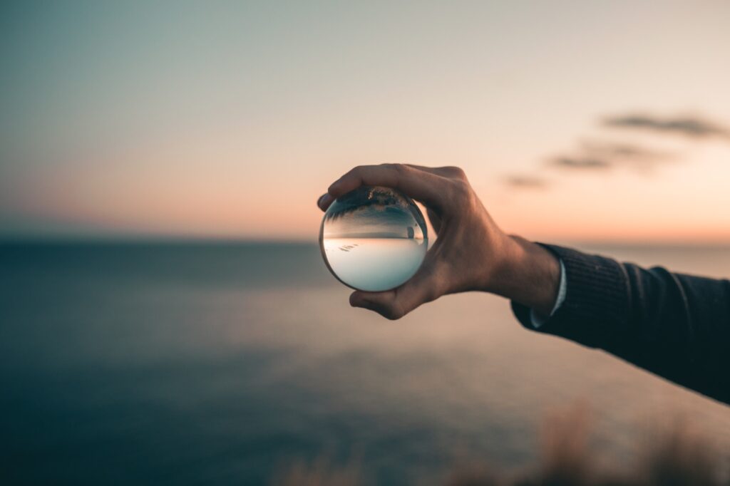 A person holds a crystal ball in their hand, capturing an inverted view of the sunrise over the sea. The ocean and horizon appear curved within the sphere, with a soft focus background showcasing hypnotherapy in Northeast England.
