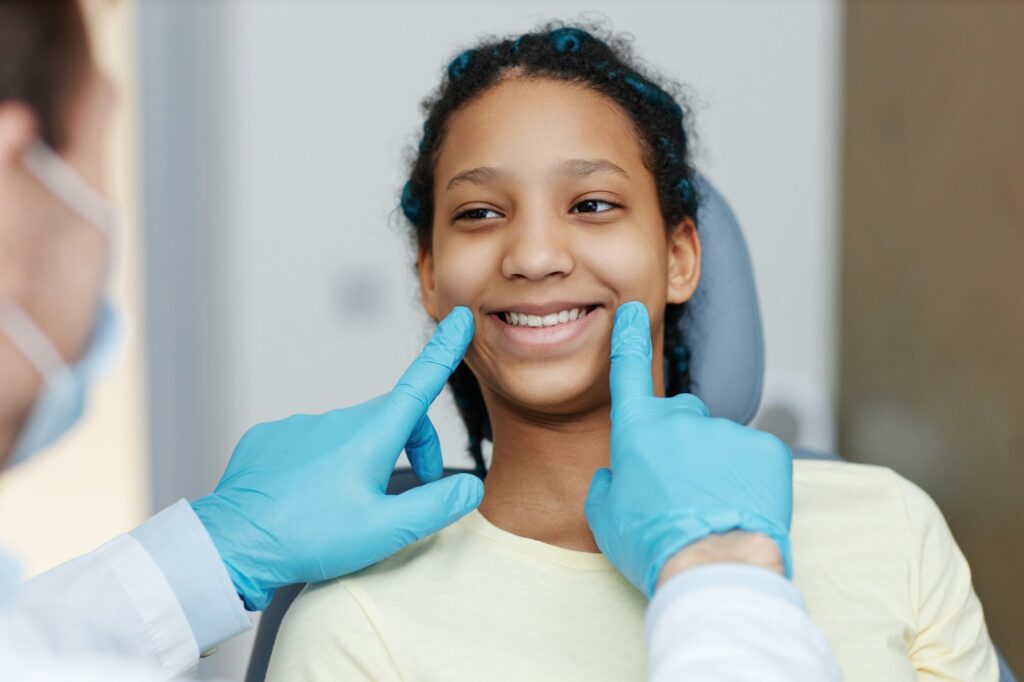 Teen black girl with toothy smile sitting in a dental chair at dentistry clinic