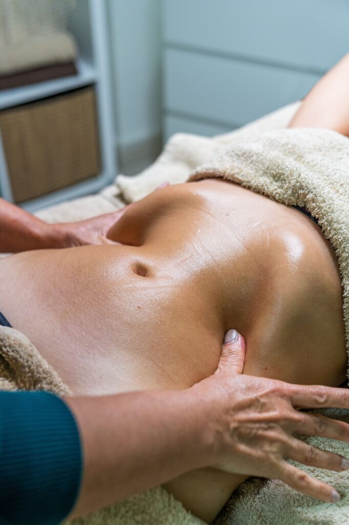 Hands of specialist performing lymphatic drainage massage on abdomen of female patient.