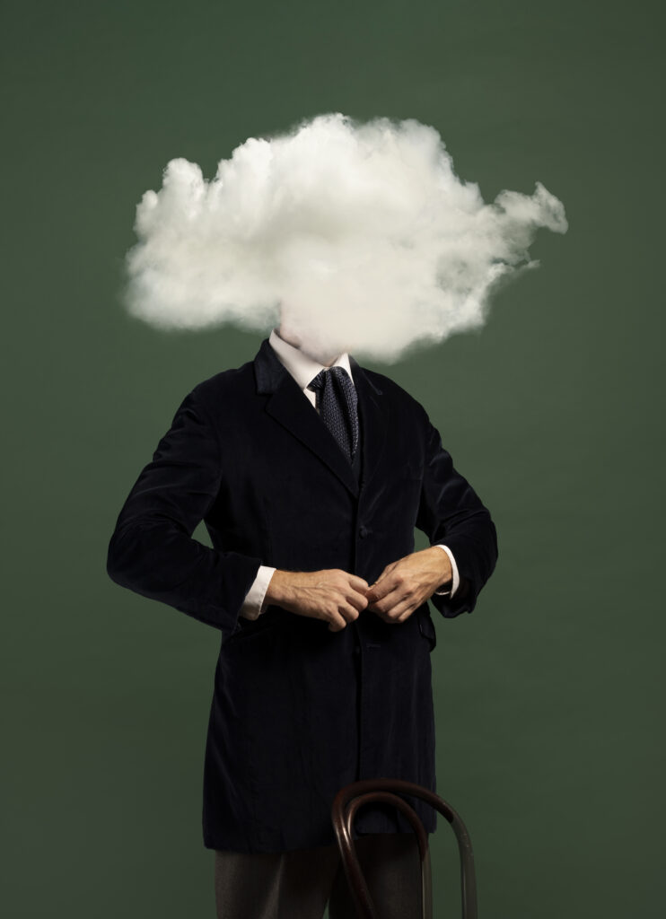 A person in a suit stands against a dark green background, buttoning their jacket. Instead of a head, an overthinking white cloud obscures their face, suggesting emotional awareness, feeling misunderstood