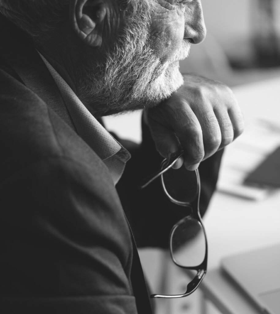 Black and white image of an older man with a beard, wearing a suit, resting his chin on his hand and holding spectacles. He appears to be looking thoughtfully into the distance, as if reflecting on hidden wisdom or feeling misunderstood.